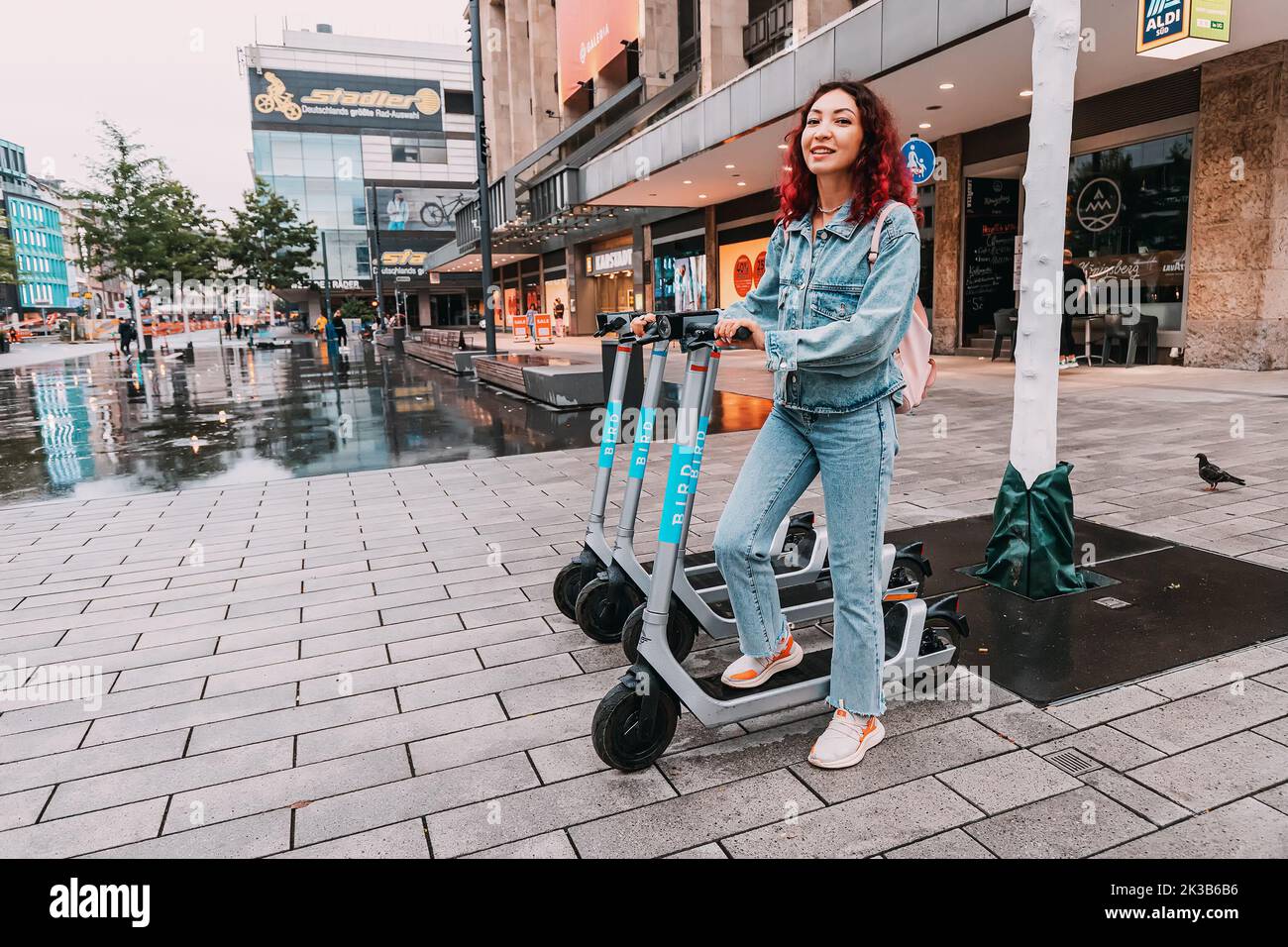 21 July 2022, Dusseldorf, Germany: The girl rents an electric scooter for move around the city. Uses a smartphone app to pay. Choose eco transport Stock Photo