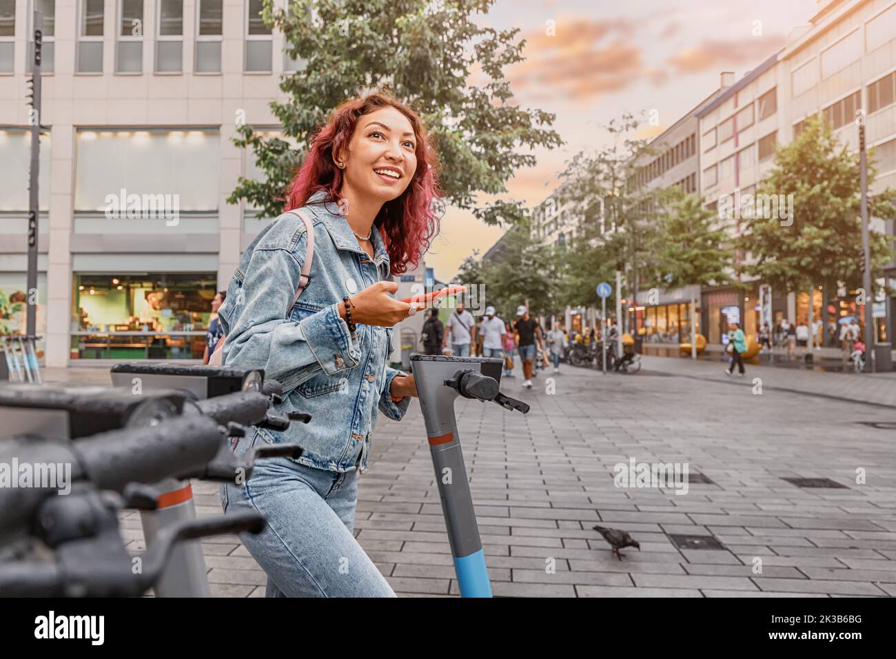 Happy girl rents an electric scooter for move around the city. Uses a smartphone app to pay. Choose eco transport Stock Photo