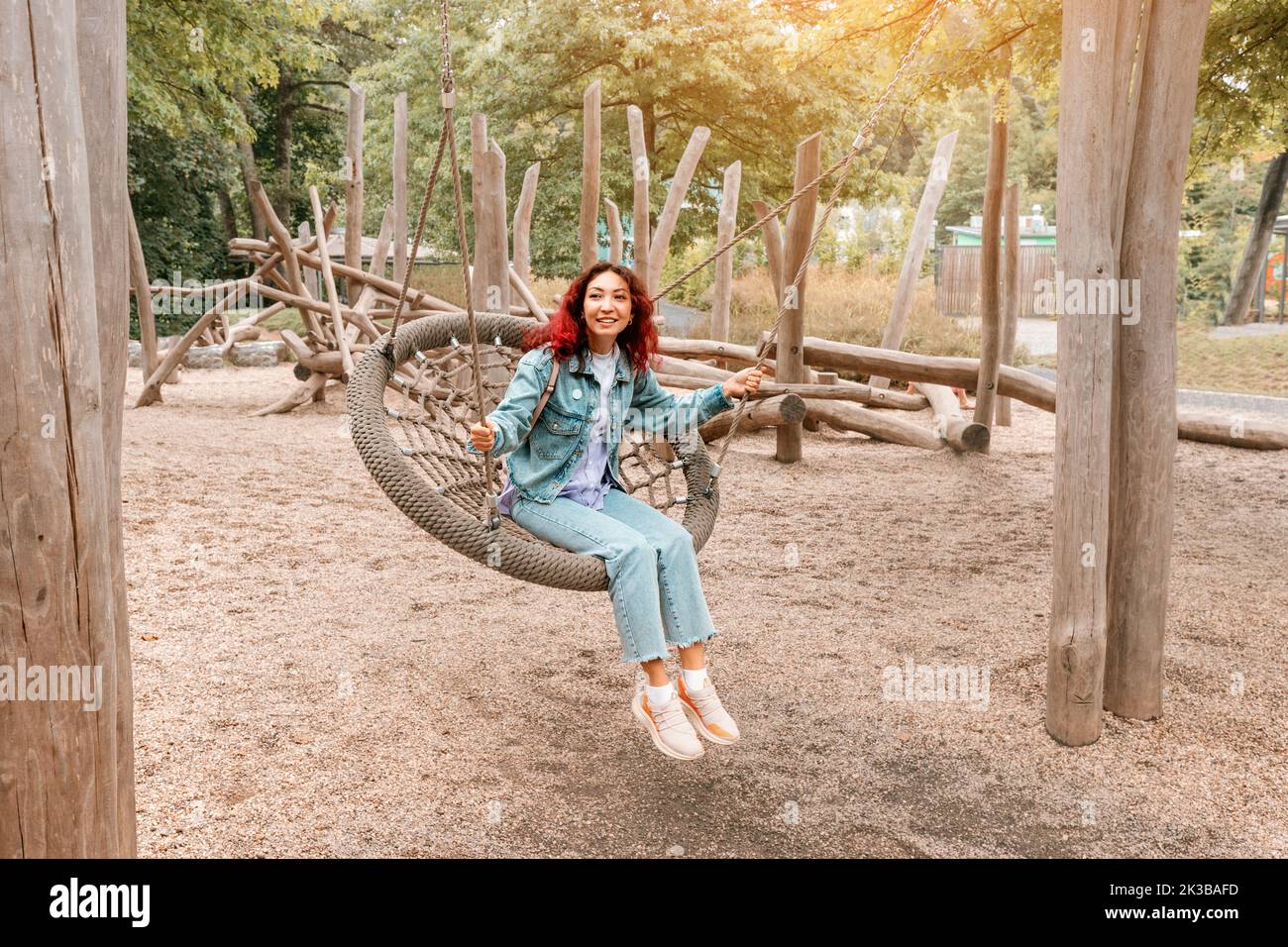 Happy girl has fallen into childhood, has fun and rides on a swing on the playground for children. Infantilism and the psychology of personality and j Stock Photo