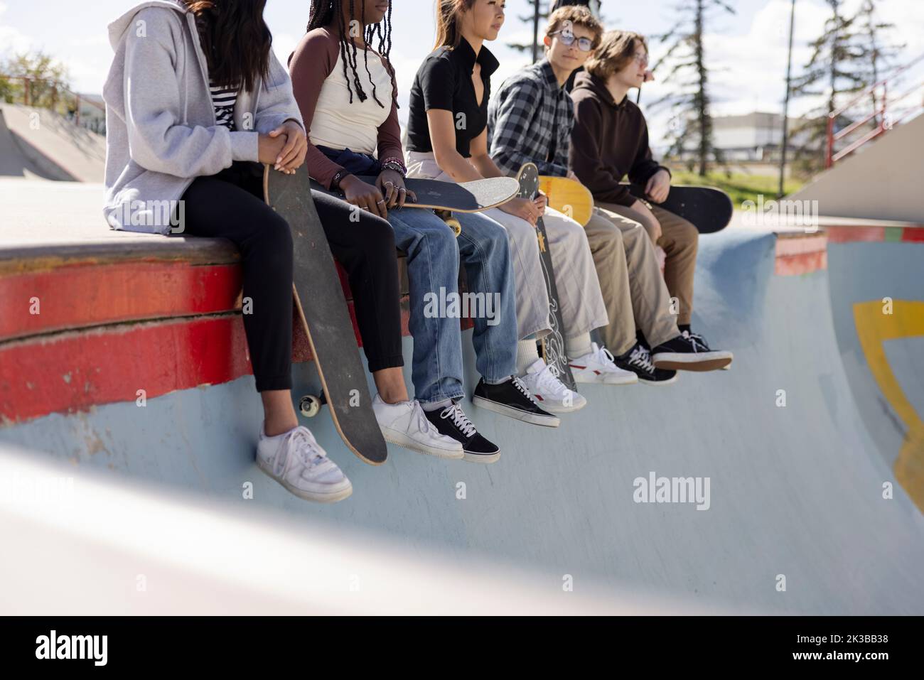 Multiethnic teen skaters sitting on edge of skatebowl Stock Photo