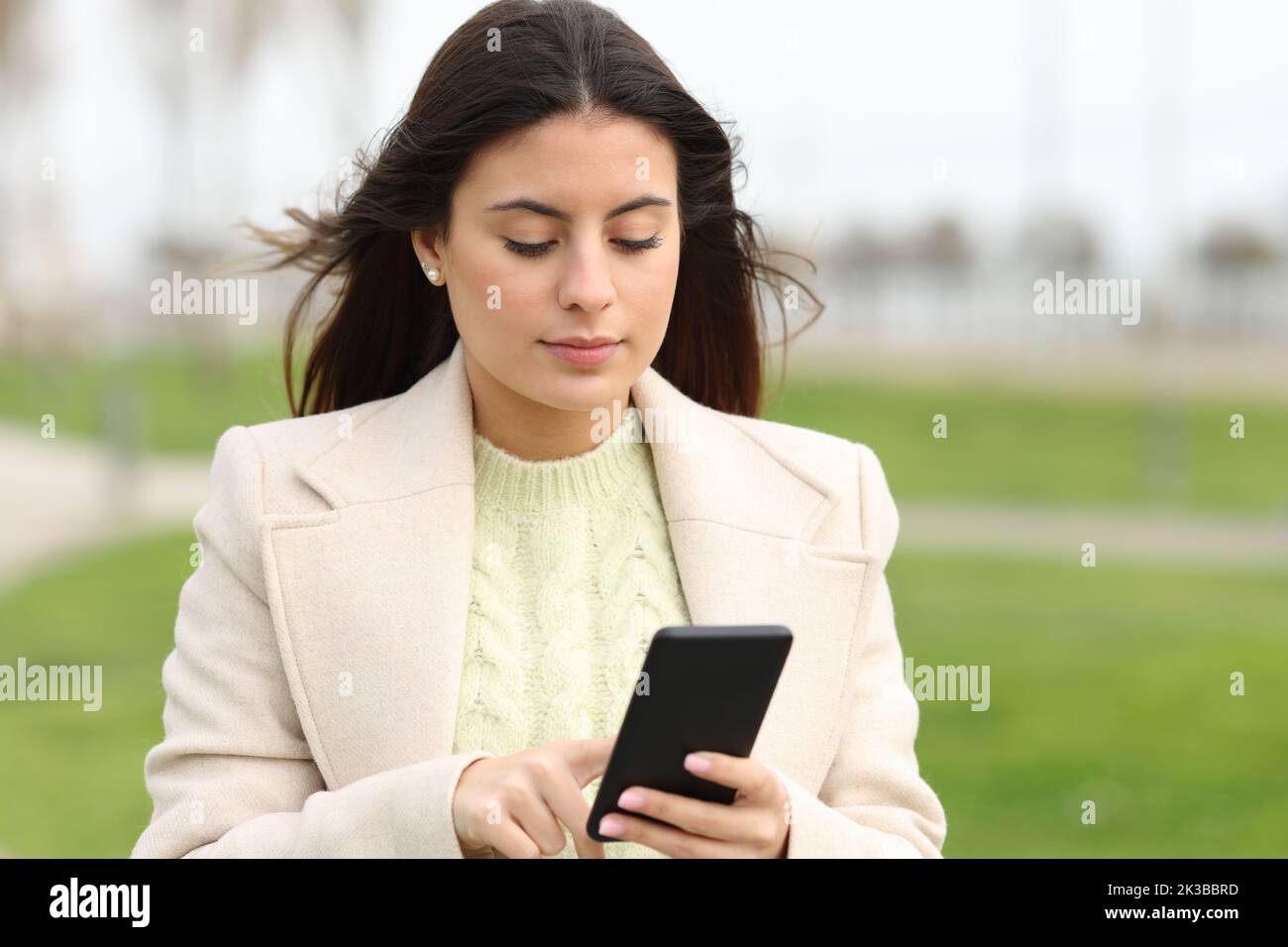Serious woman walking using smart phone in a park in winter Stock Photo