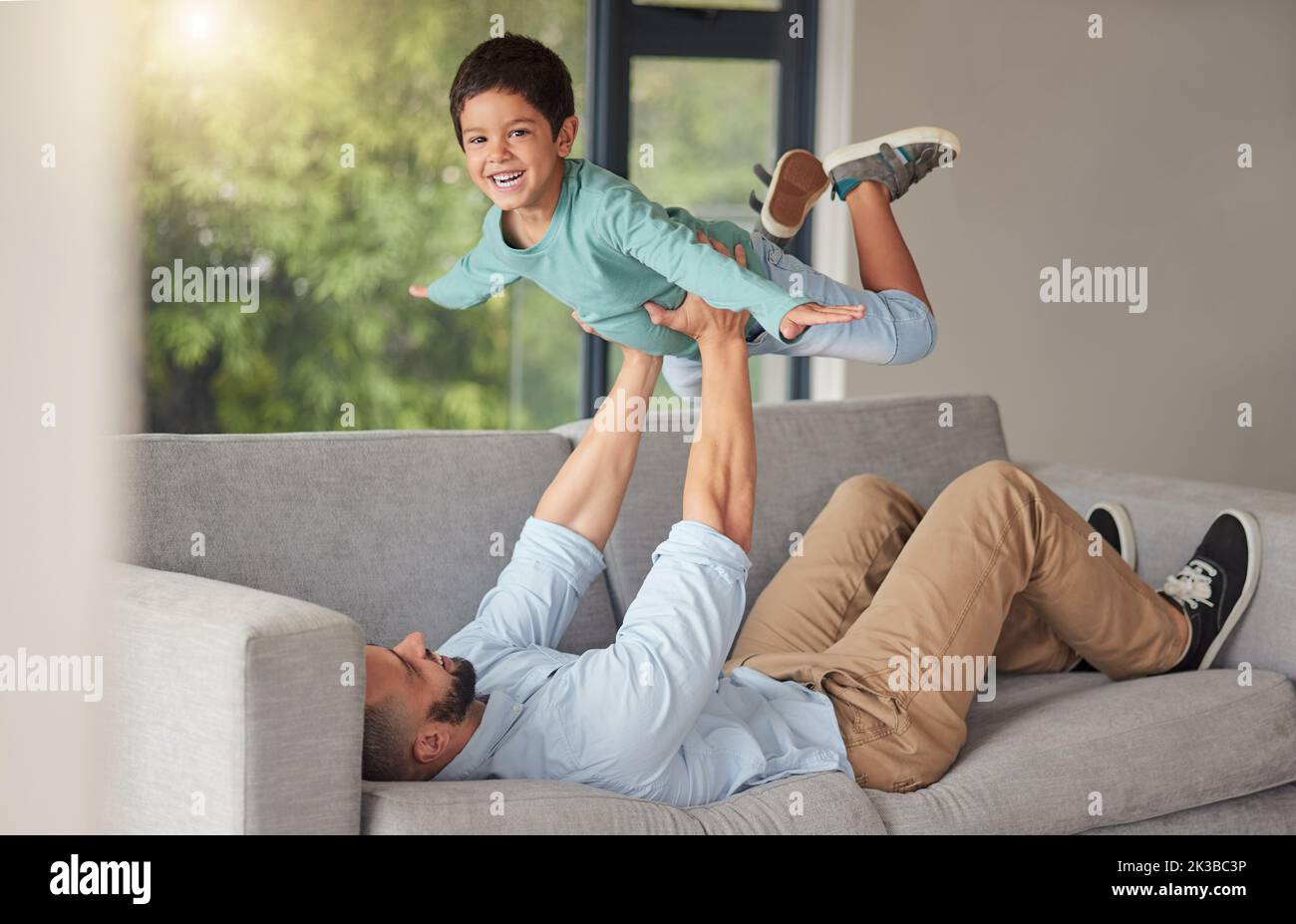 Happy family, love and father and son bonding on a sofa at home, playing and being creative with a fun game. Energy, fantasy and airplane pose by Stock Photo
