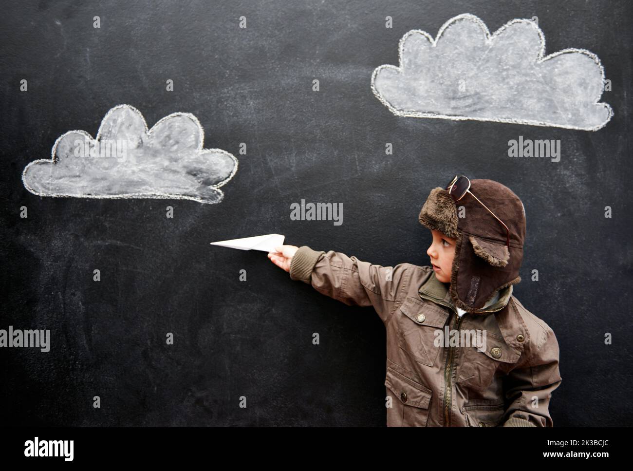 Ladies and gentlemen, this is your captain speaking...a little boy playing with an airplane in front of clouds drawn on a blackboard. Stock Photo
