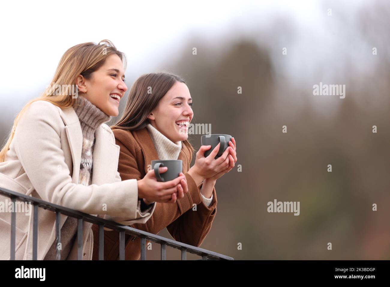 Two happy friends talking and drinking in a balcony in winter Stock Photo