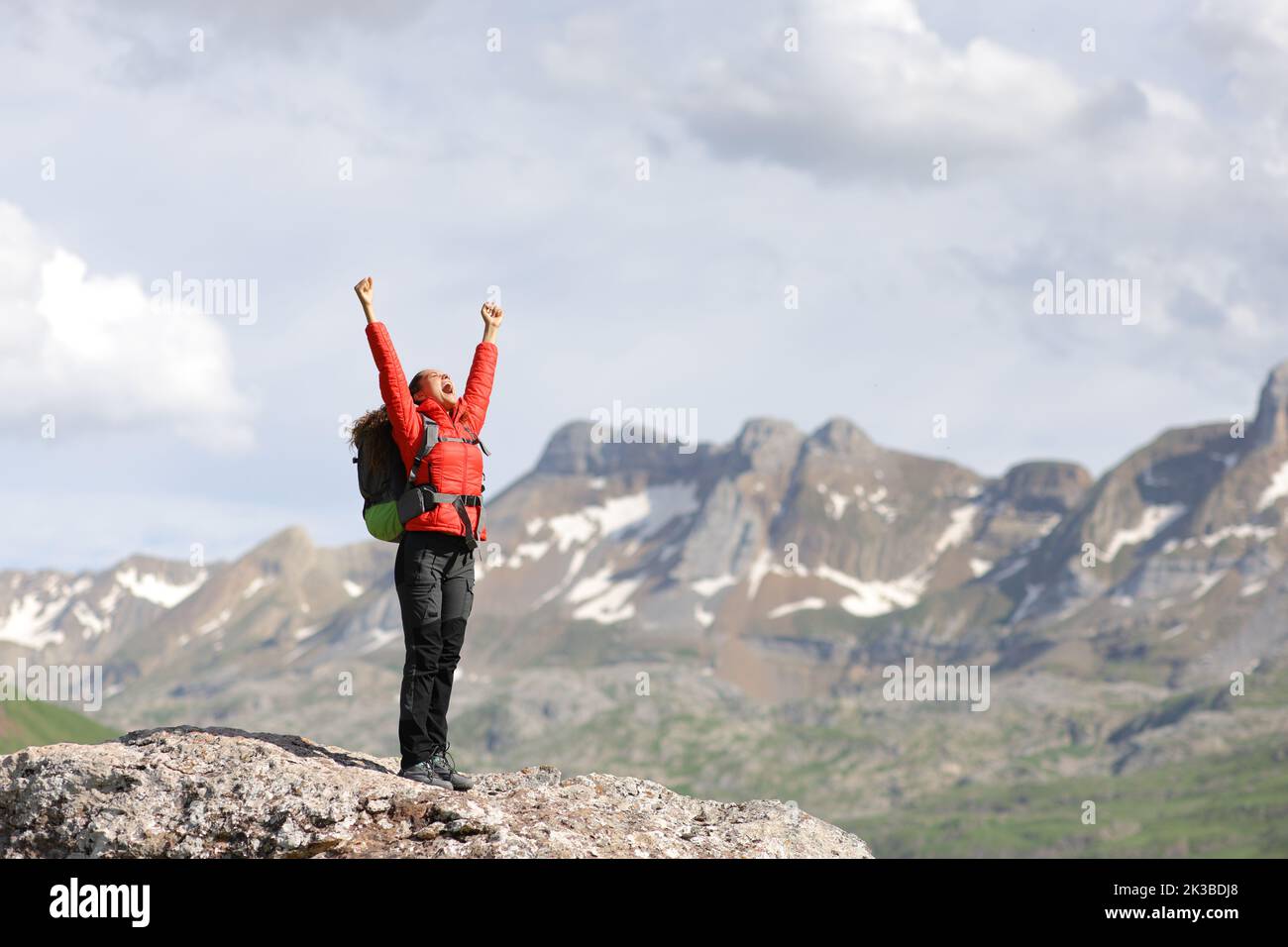 Full body portrait of a hiker in red raising arms celebrating in a high mountain Stock Photo