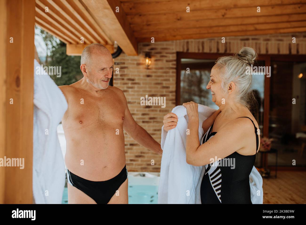 Senior couple standing in terrace and preparing for outdoor bathing, putting off bathrobes, during cold winter day. Stock Photo