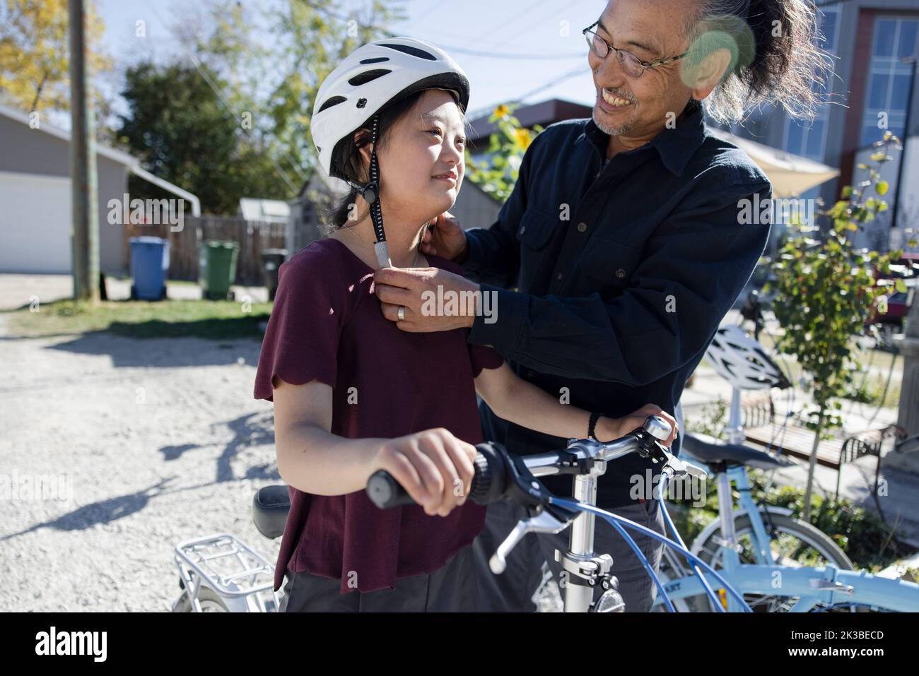 Father helping daughter with Down Syndrome put on bike helmet Stock