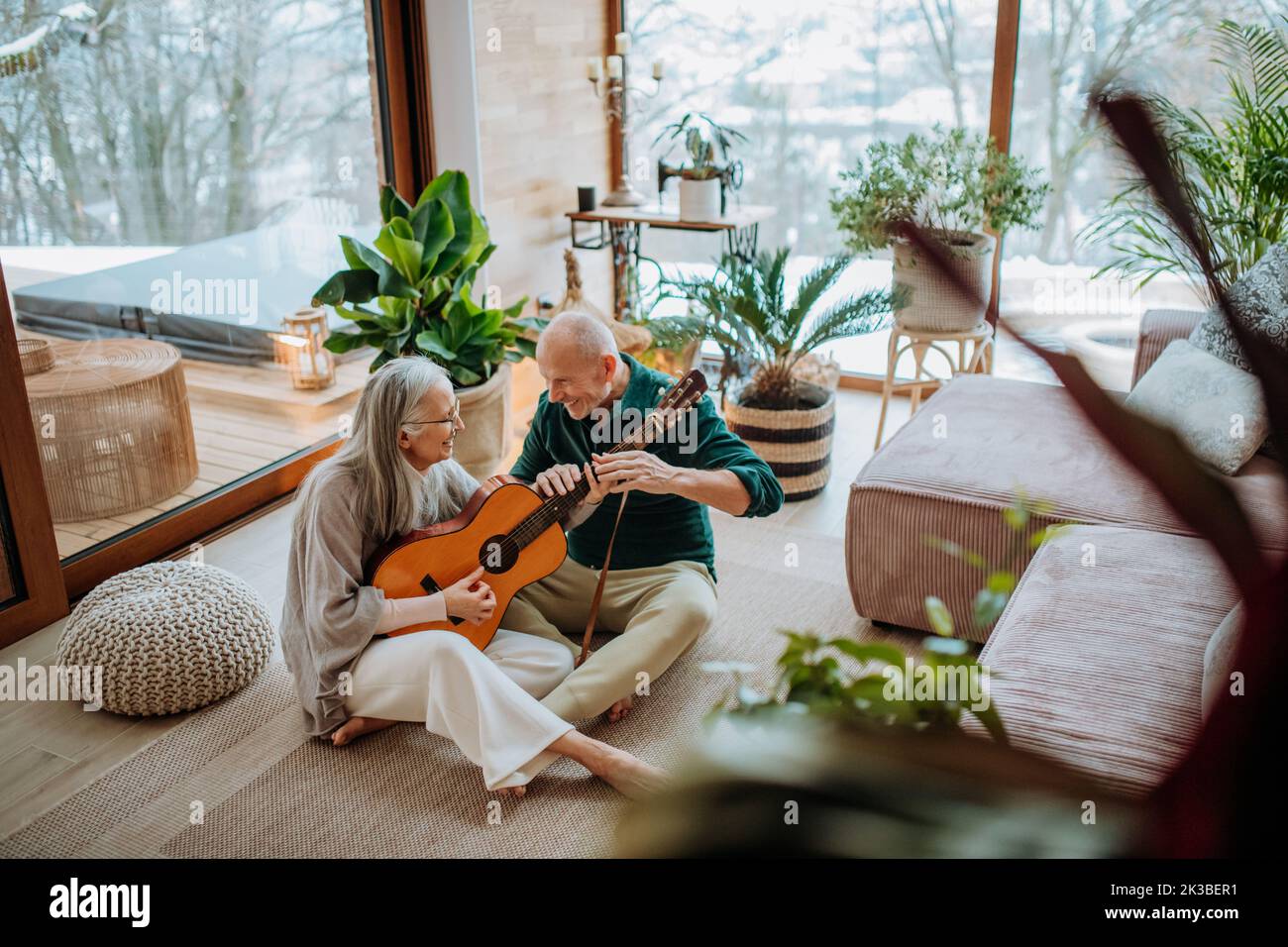 Senior couple playing on guitair, sitting in cozy living room and enjoying autumn day. Stock Photo
