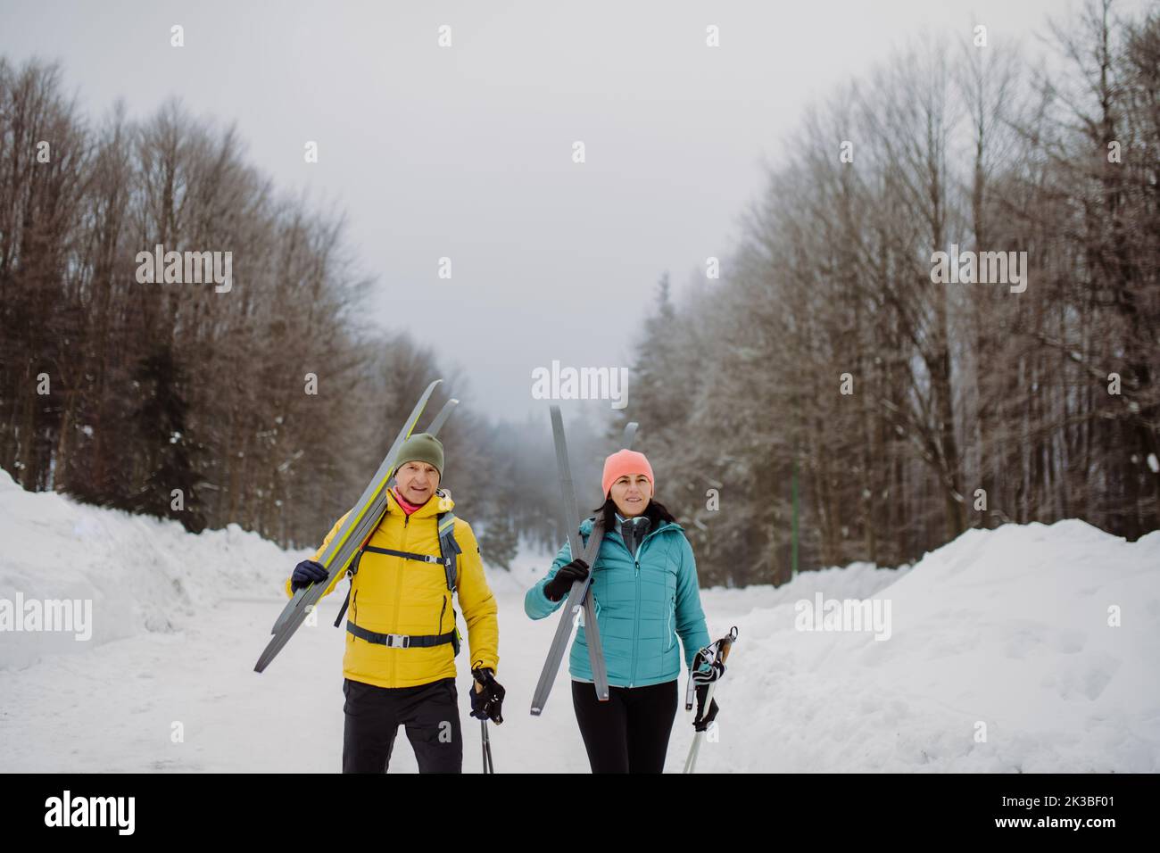 Senior couple crossing forest with skis on shoulders. Stock Photo