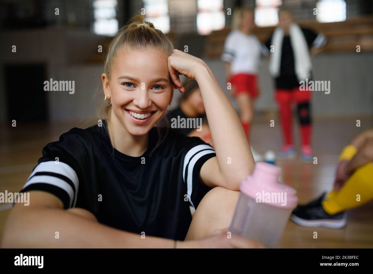 Portrait of young woman, sports team players in gym sitting and resting after match with her teammates. Stock Photo