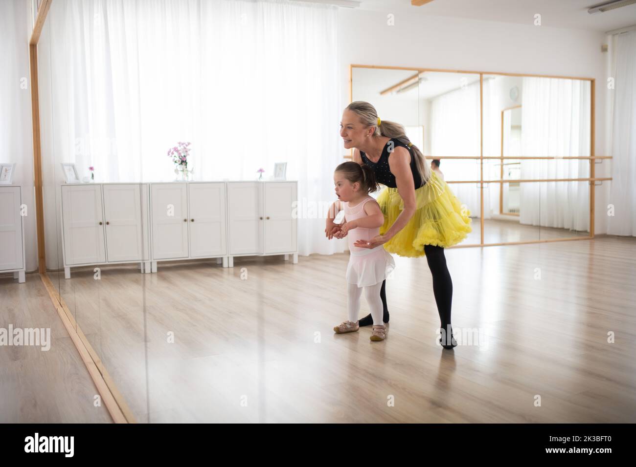 Little girl with down syndrome learning ballet with dance lecteur in ballet studio. Stock Photo