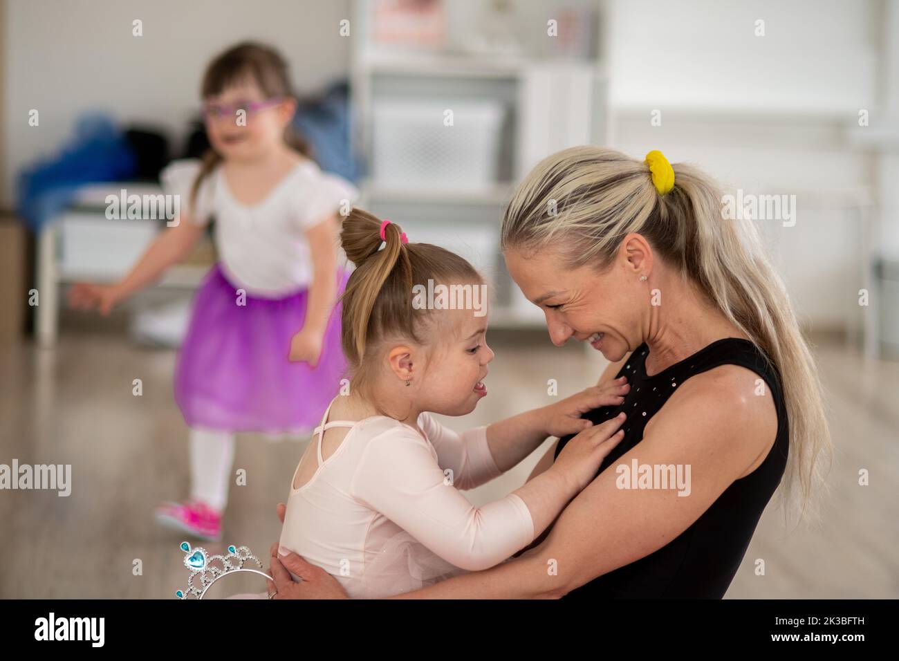 Little girl with down syndrome cuddling with her mother during ballet class. Concept of integration disabled children and parenthood. Stock Photo
