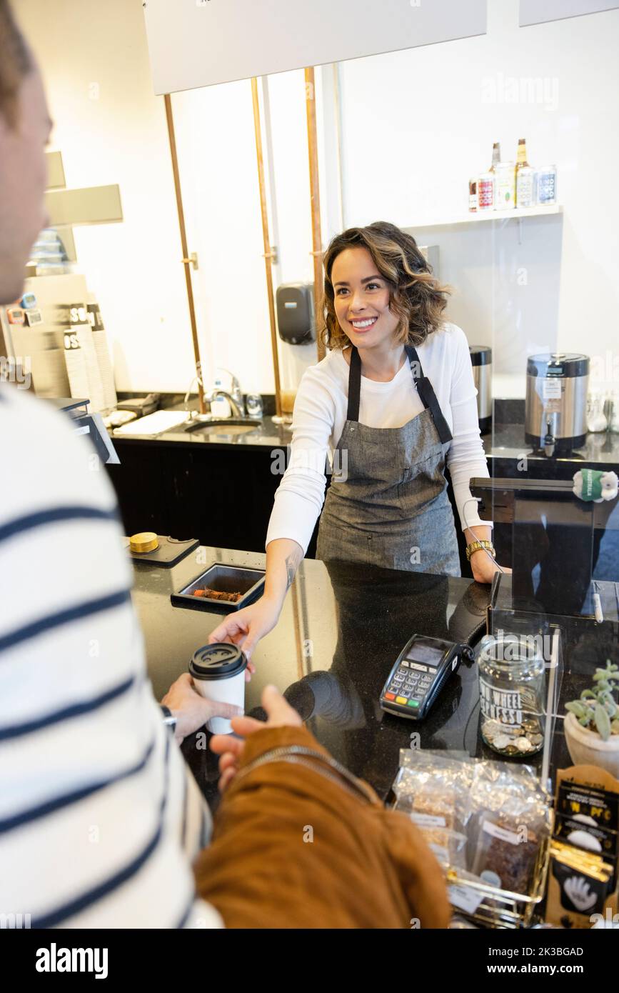 Friendly female cafe owner serving coffee to customer behind counter Stock Photo Alamy