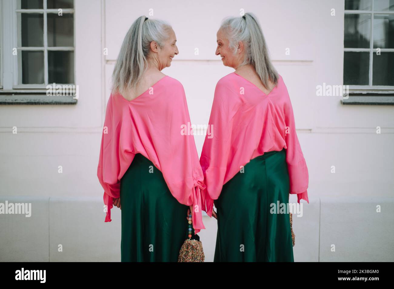 Senior women twins in colourful clothes in city, shopping.Rear view. Stock Photo