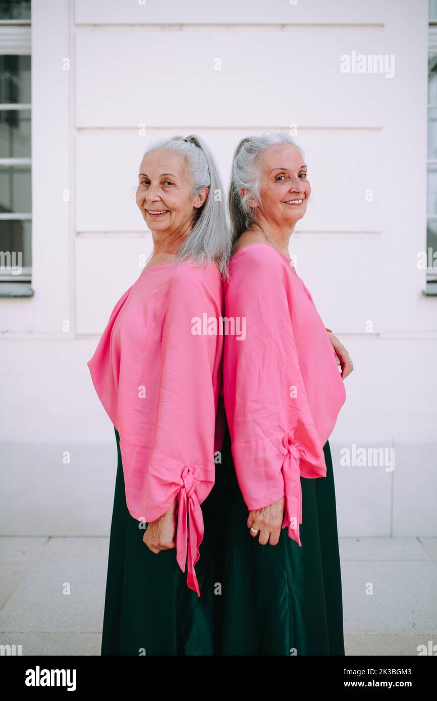 Side view of senior women, twins,in same clothes standing back to back, outdoor in city. Stock Photo