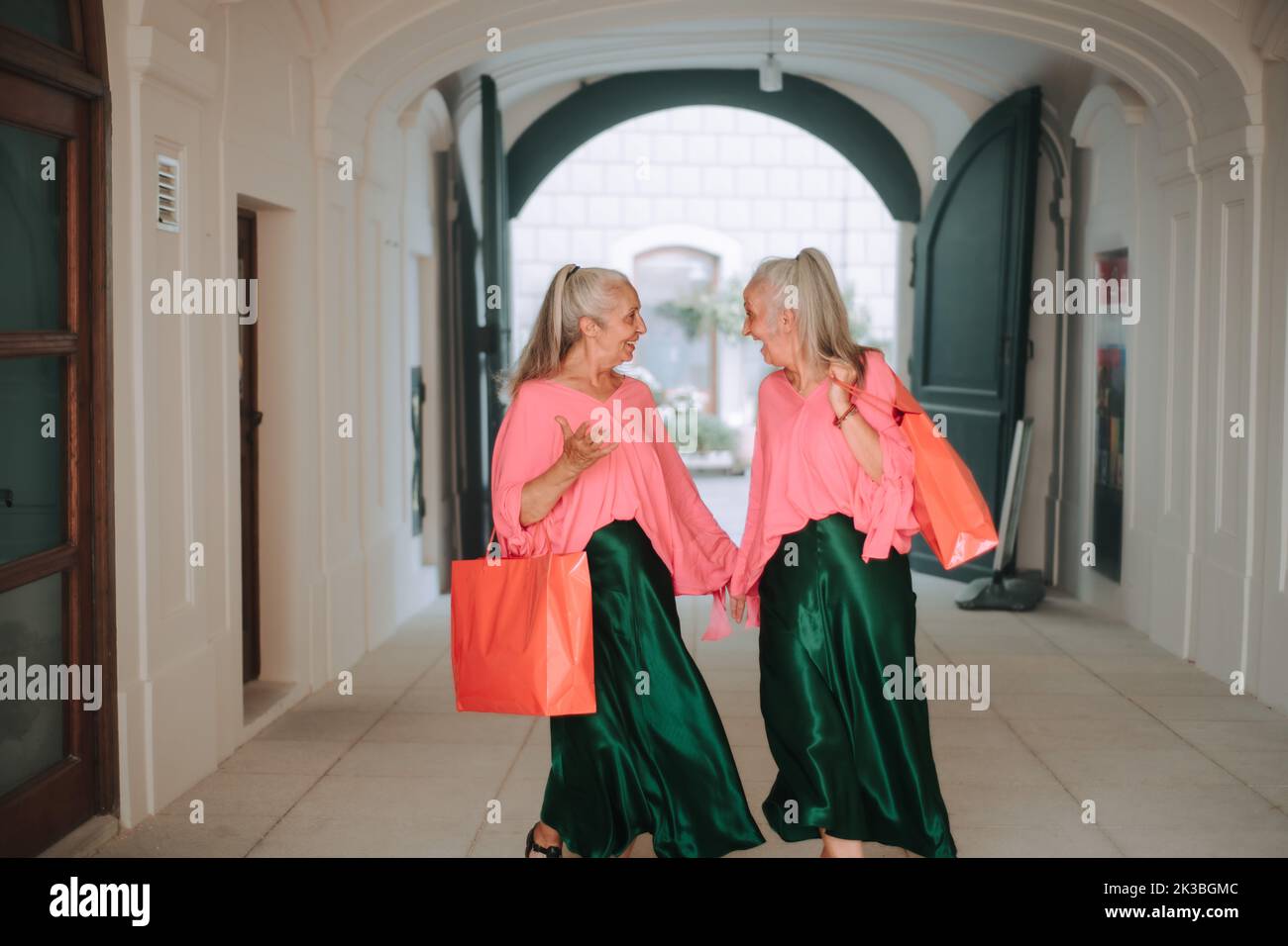 Happy senior women twins in colourful clothes in city, shopping. Stock Photo