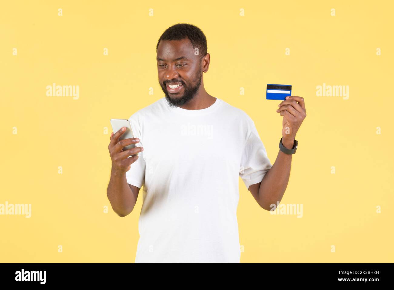Black Guy Using Smartphone And Credit Card Shopping, Yellow Background Stock Photo