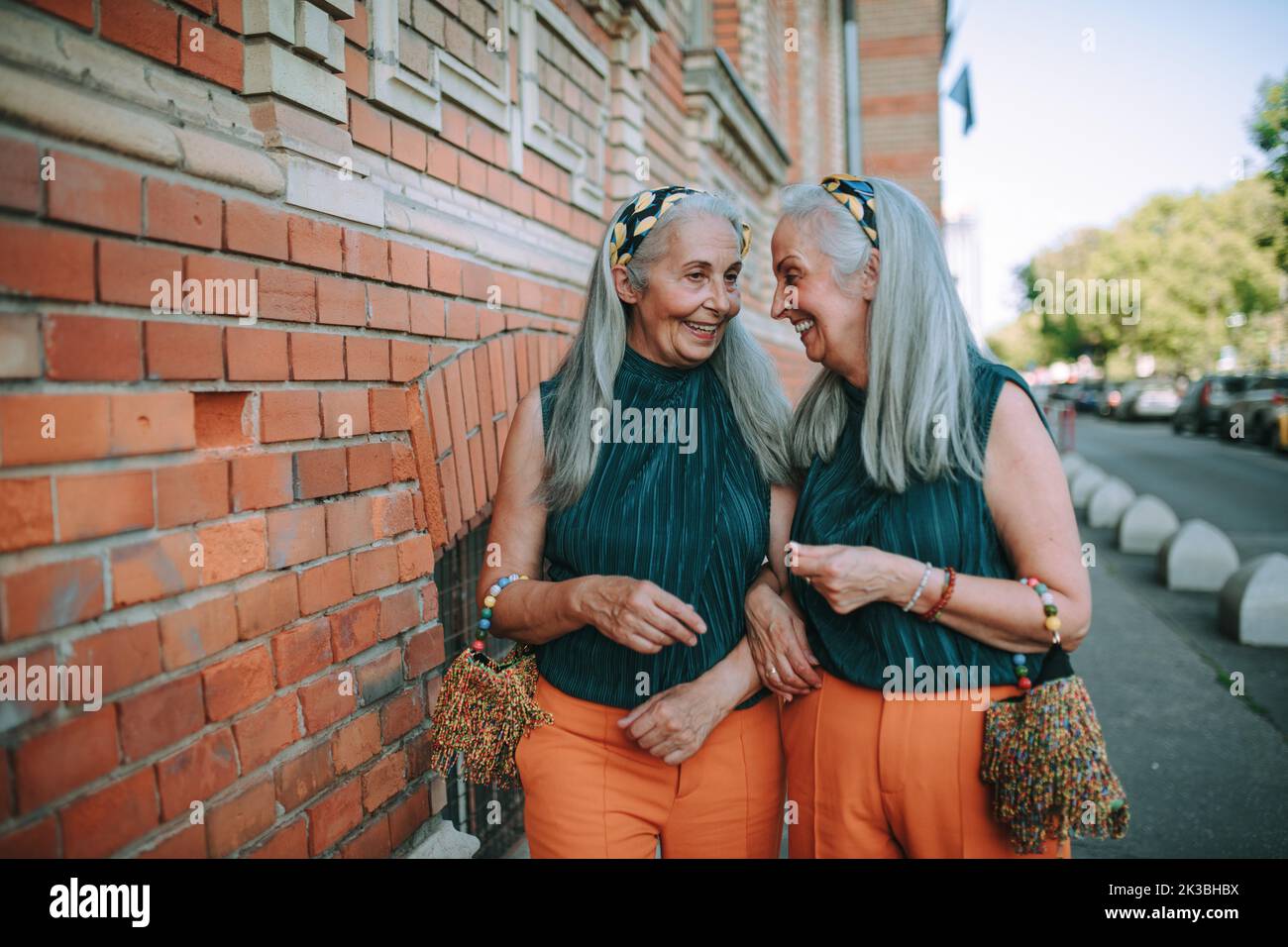 Happy senior twins in same clothes talking and walking in city. Stock Photo