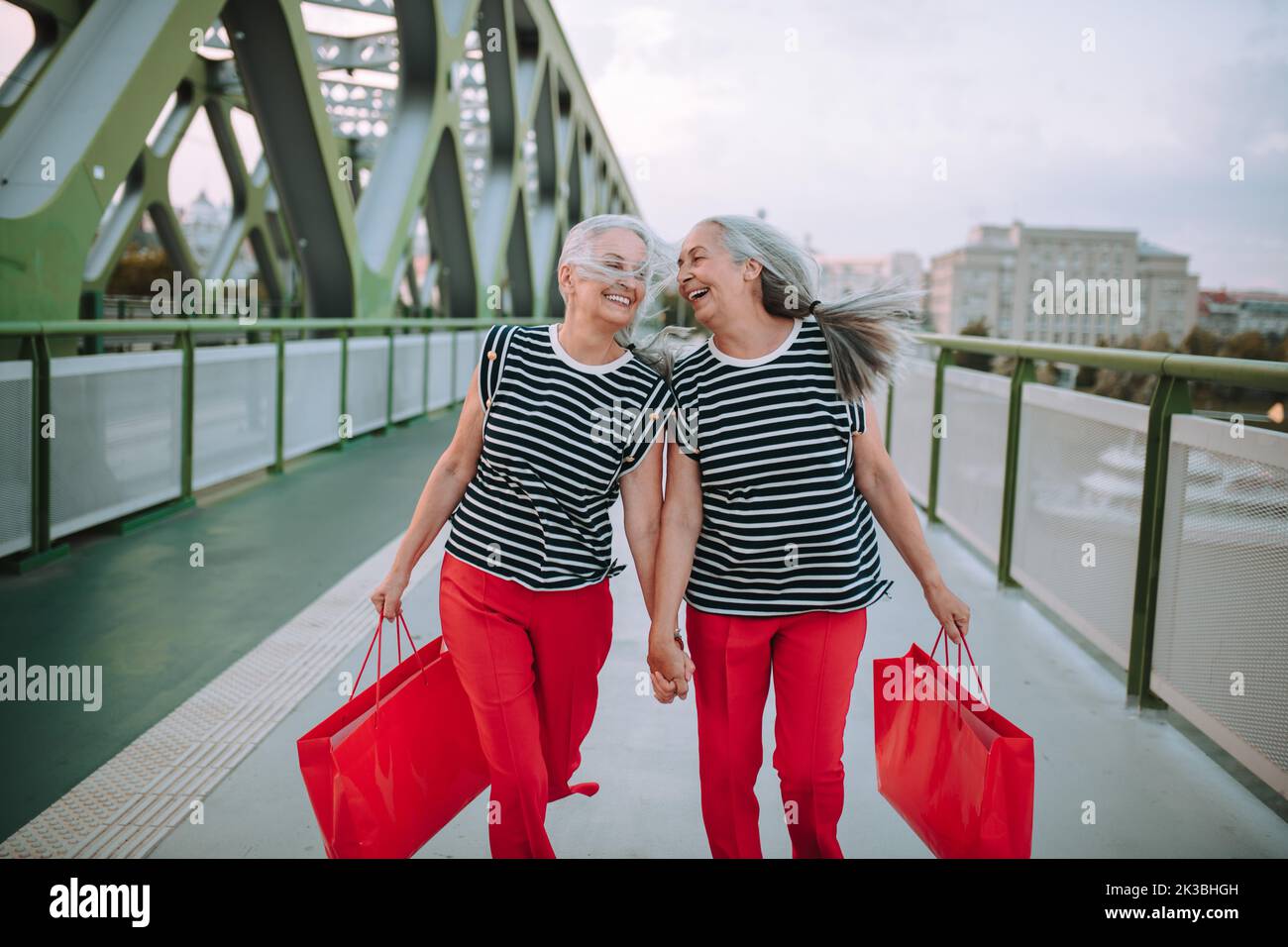 Happy senior twins in same clothes walking in city, returning from shopping. Stock Photo