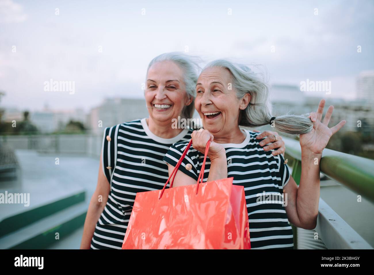 Happy senior twins in same clothes walking in city, returning from shopping. Stock Photo
