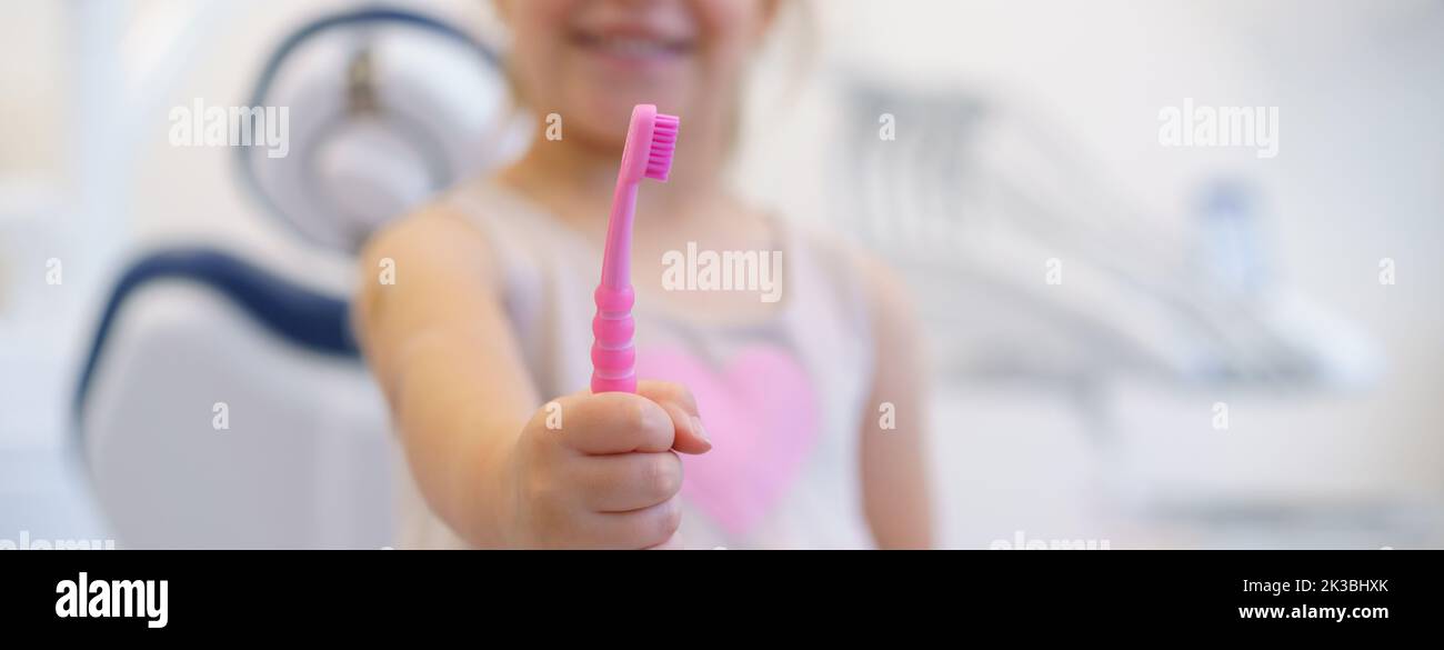 Close-up of little girl holding pink tootbrush, concept of children oral hygiene,prevention and dental health. Stock Photo