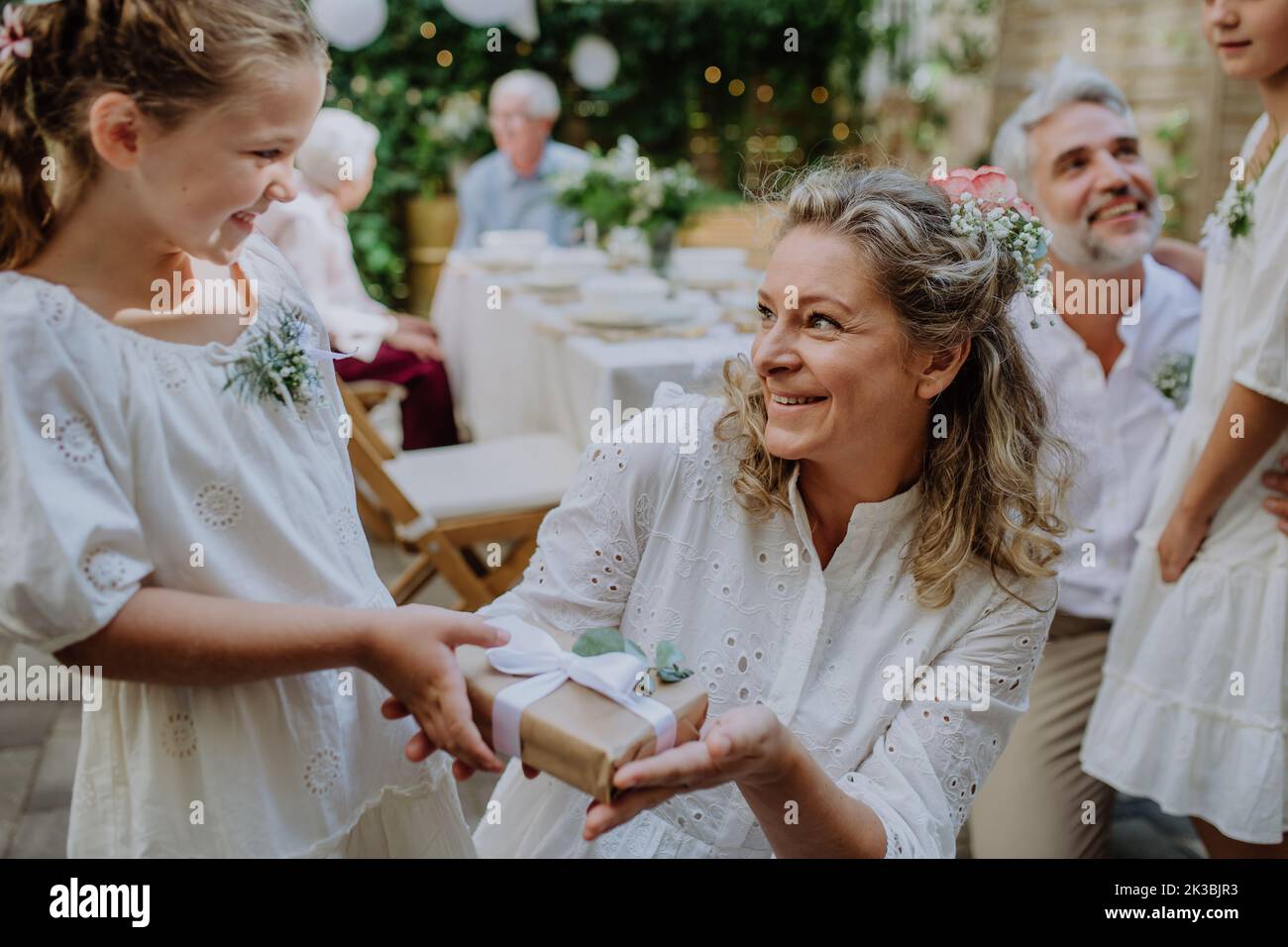 Little girl giving wedding gift to mature bride at wedding backyard party. Stock Photo