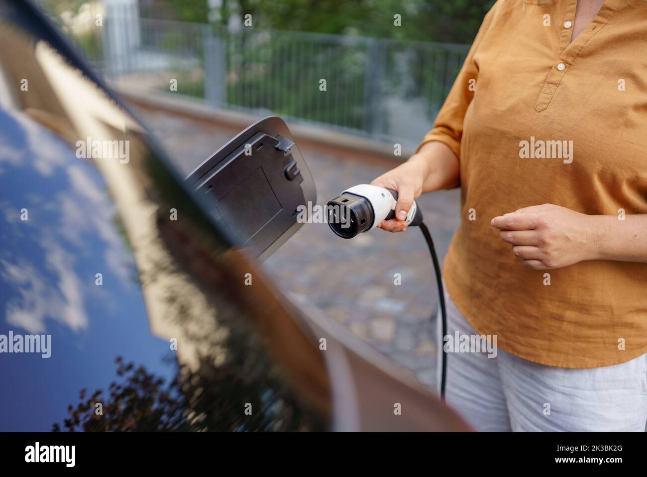Woman holding power supply cable at electric vehicle charging station, closeup Stock Photo