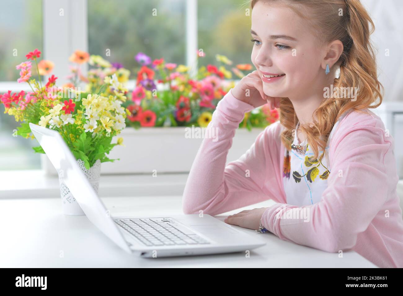 Teenage girl sitting at a table with a laptopt at home. Stock Photo