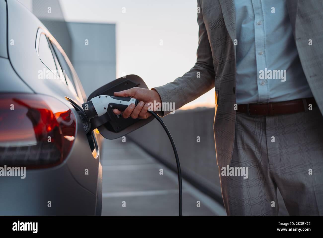 Man holding power supply cable at electric vehicle charging station, closeup Stock Photo