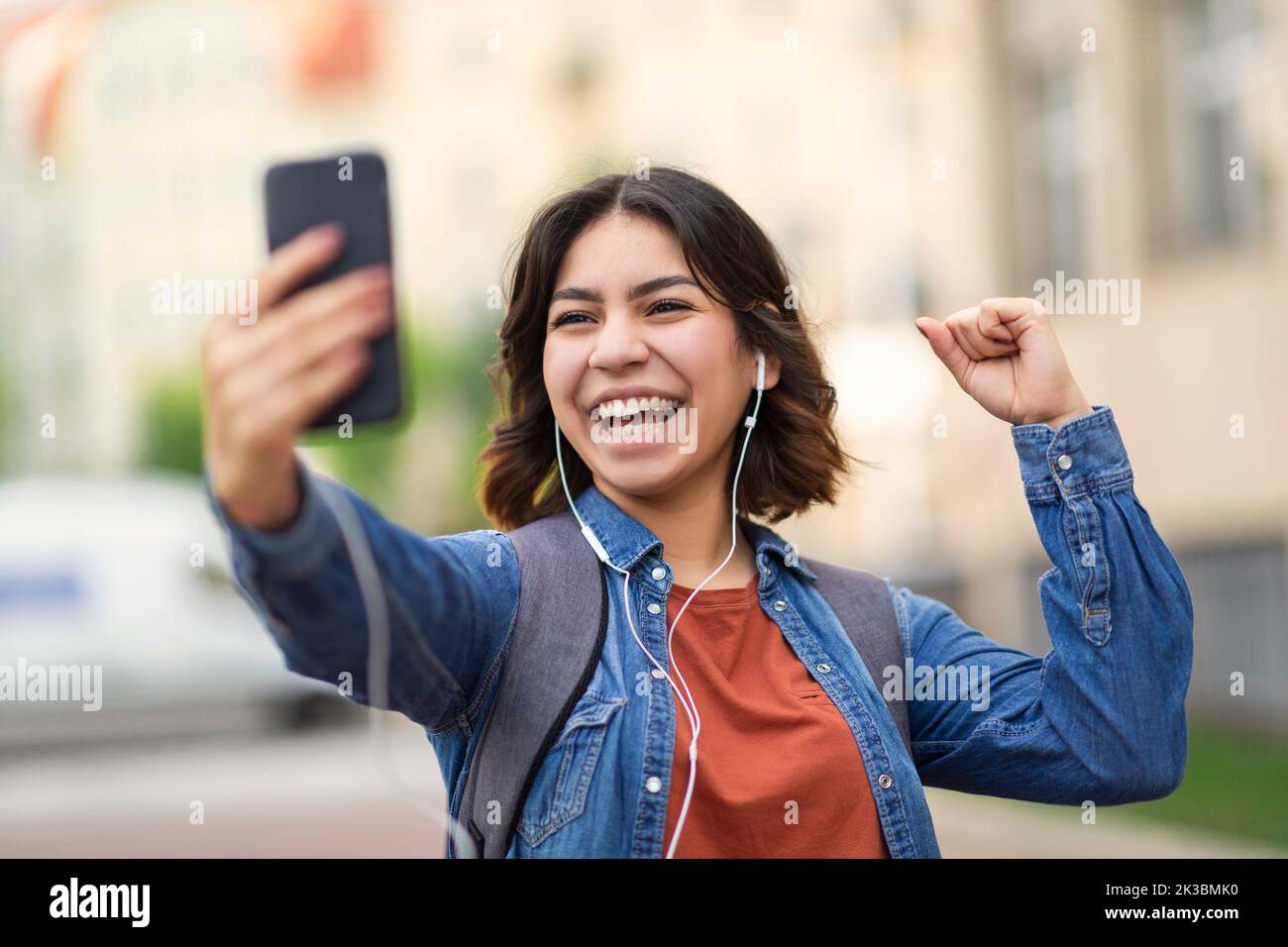 Overjoyed arab female student holding smartphone and celebrating success outdoors Stock Photo