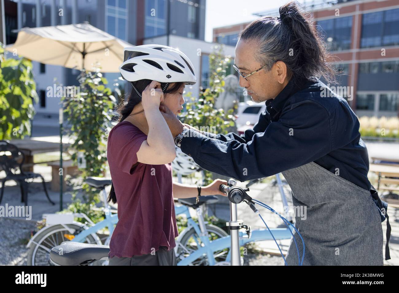 Father helping daughter with Down Syndrome put on bicycle helmet Stock