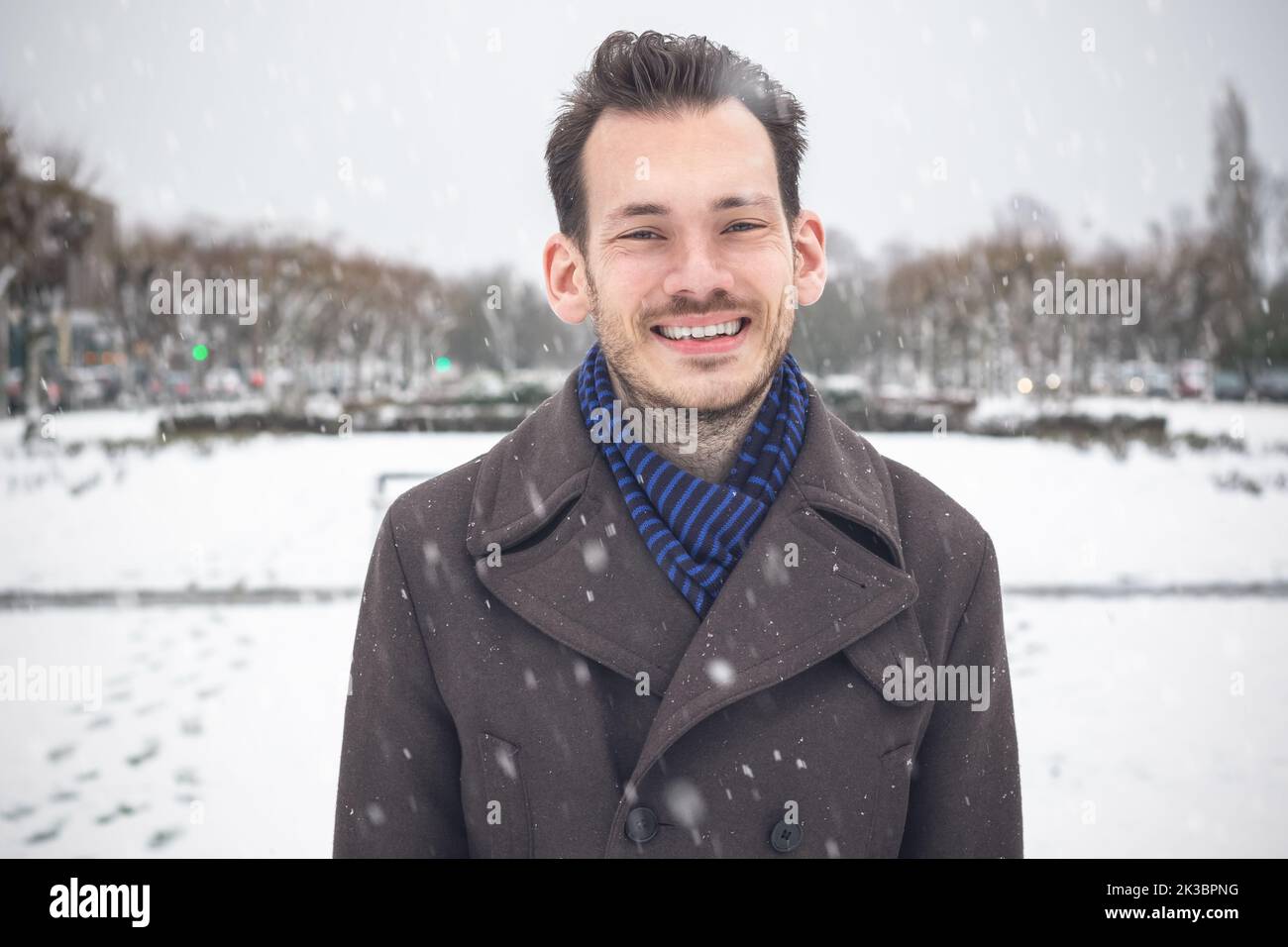 Portrait of young handsome man with beard smiling laughing looking at camera in winter snow Stock Photo