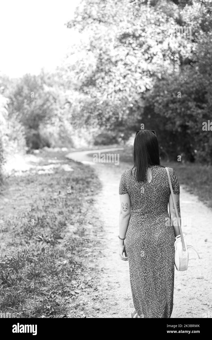 Grayscale photo of a woman walking by a path through the forest Stock ...