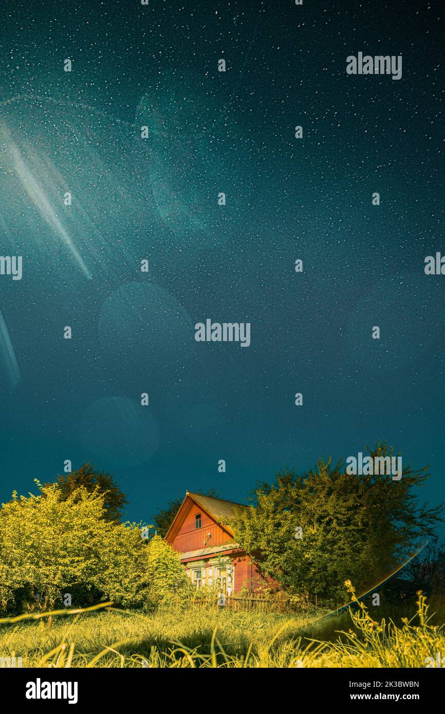 Night sky over house in village. Night starry sky above house with bright stars and meteoric track trail. Glowing stars above summer nature Stock Photo