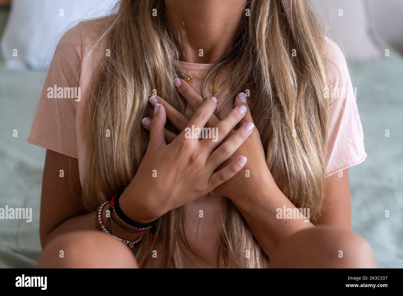 A heartbroken woman holding her chest with her hands while sitting on a bed Stock Photo
