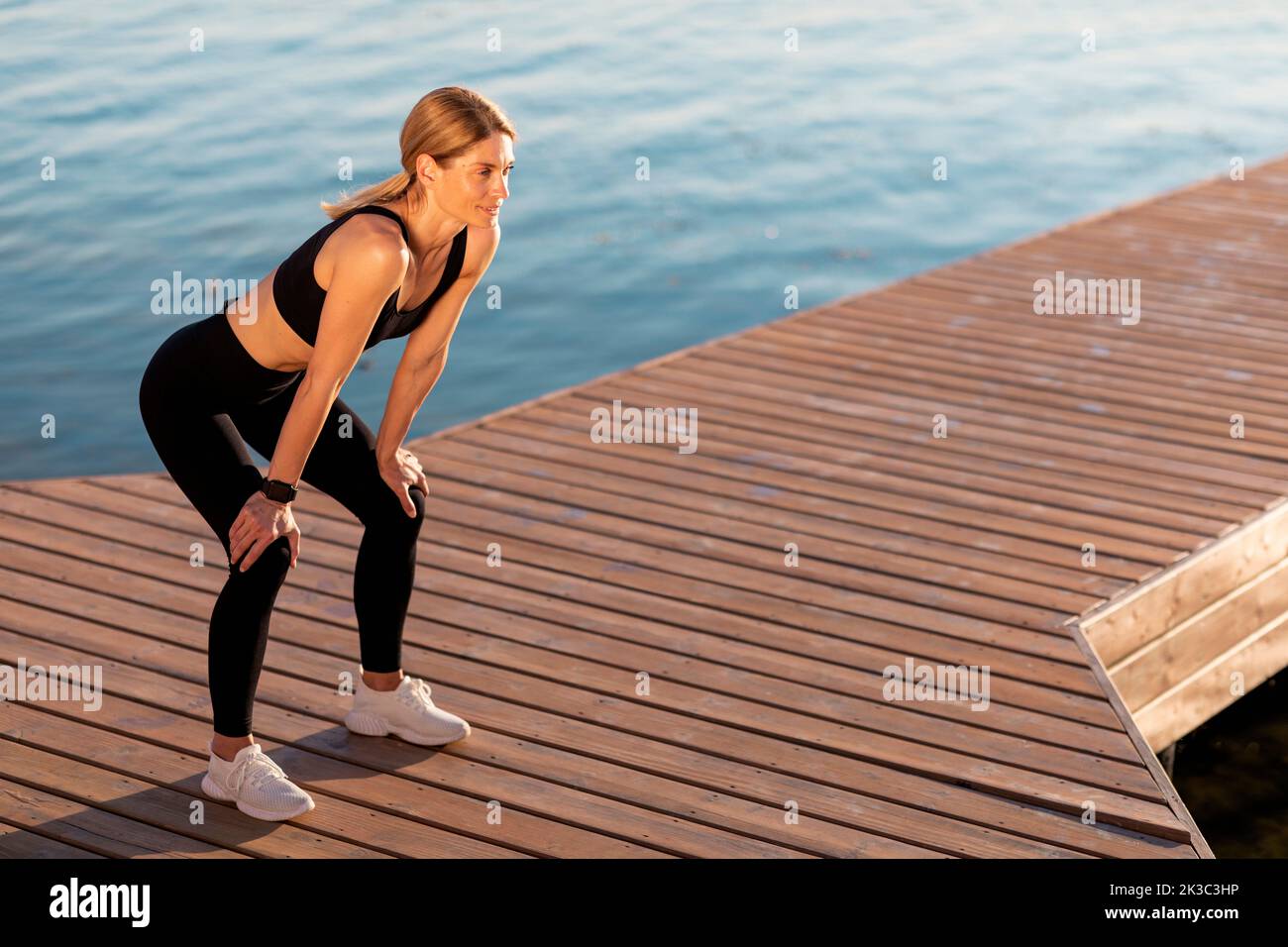 Middle Aged Female Athlete In Activewear Resting On Pier While Training Outdoor Stock Photo