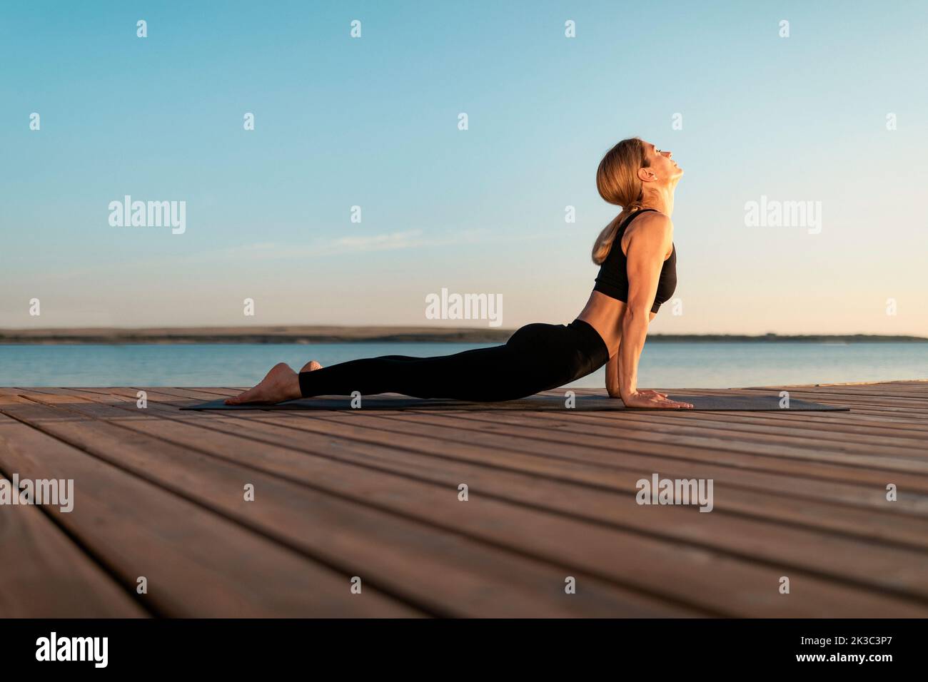 Sporty middle aged female practicing yoga outdoors, making upward facing dog pose Stock Photo