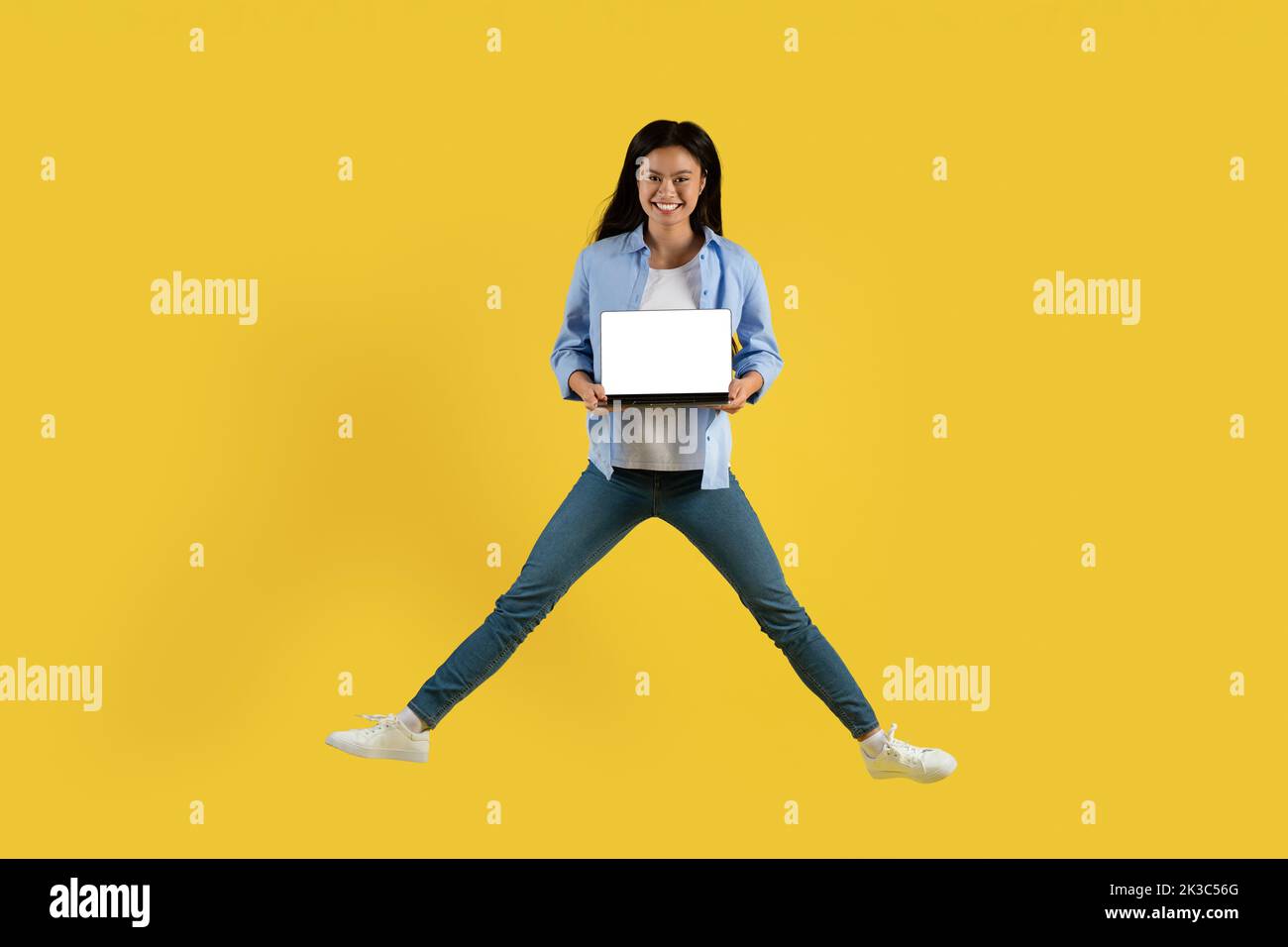 Smiling young chinese woman student in casual jumping, showing laptop