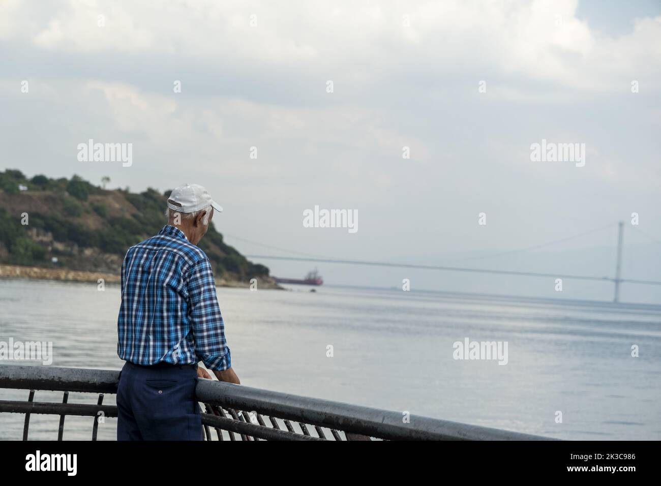 Back turned old man looking forward and trying to fishing, cinematic scene, older man's hobbies idea, calm and relaxed scene, bridge and mountain Stock Photo