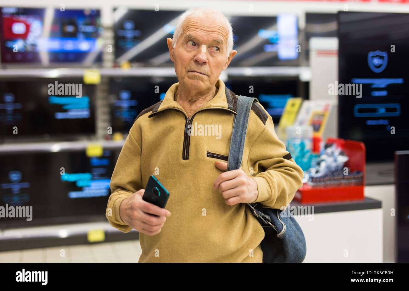 elderly grayhaired man pensioner looking counter with modern digital televisors in showroom of digital goods store Stock Photo
