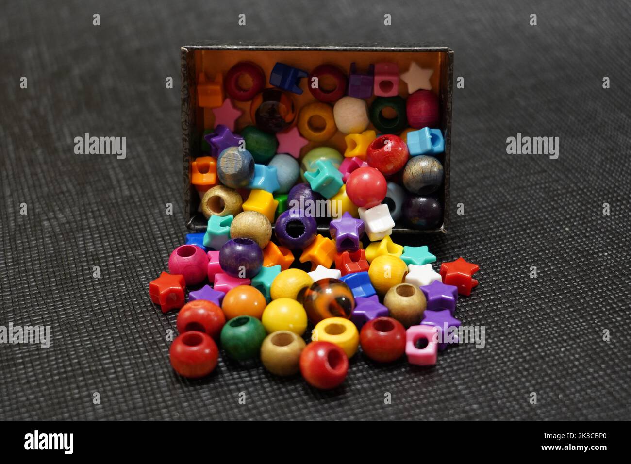 Close-up shot of colorful necklace pieces falling from a cardboard box in front of black background Stock Photo