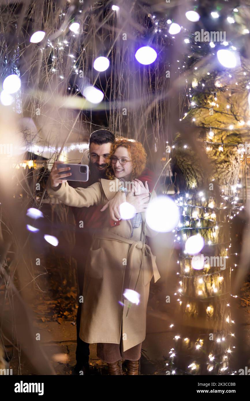 Young couple using a smartphone under beautiful Christmas lights Stock Photo