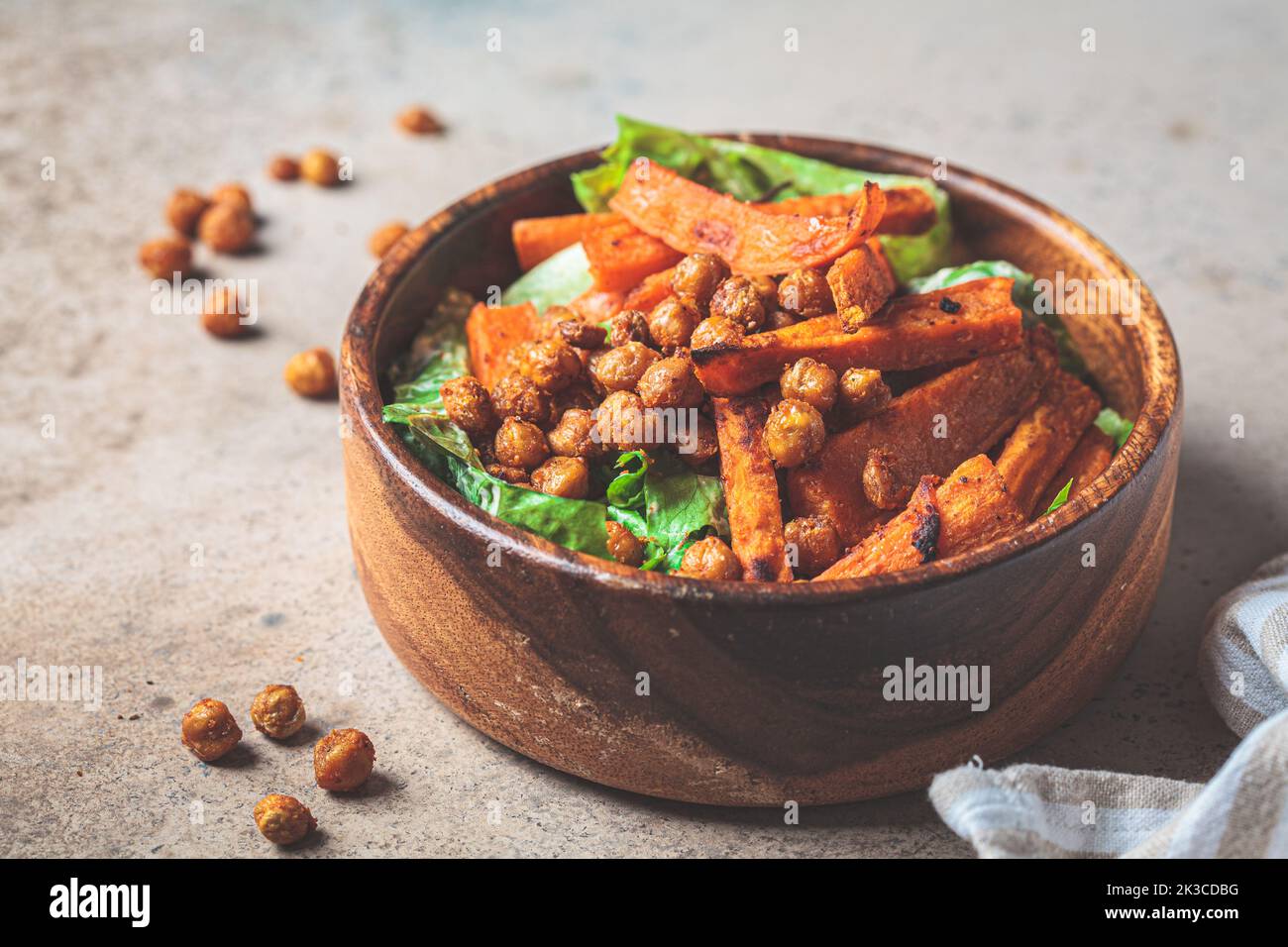 Baked sweet potato wedges and spicy fried chickpea salad in a wooden bowl. Plant based food concept. Stock Photo