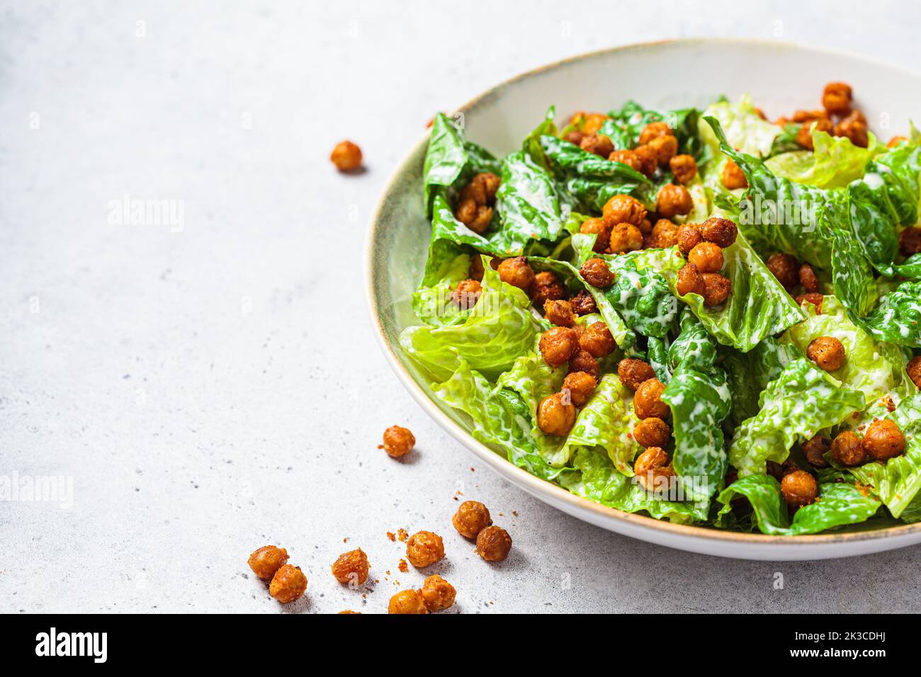 Vegan caesar salad with fried spicy chickpeas in a gray bowl, copy space. Plant based food concept. Stock Photo