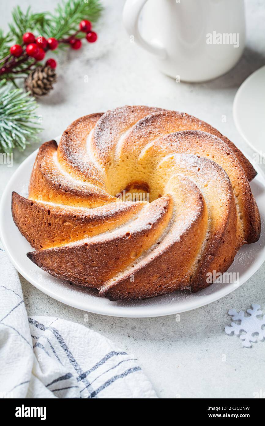 Christmas dessert, close-up. Vanilla pound cake with powdered sugar on a white plate, light gray background with Christmas tree branches. Stock Photo