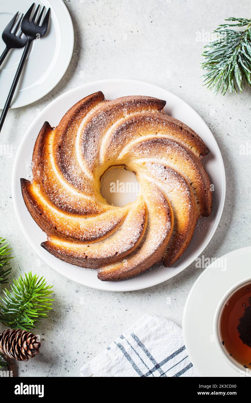 Christmas dessert, flat lay. Vanilla pound cake with powdered sugar on a white plate, light gray background with Christmas tree branches, top view. Stock Photo