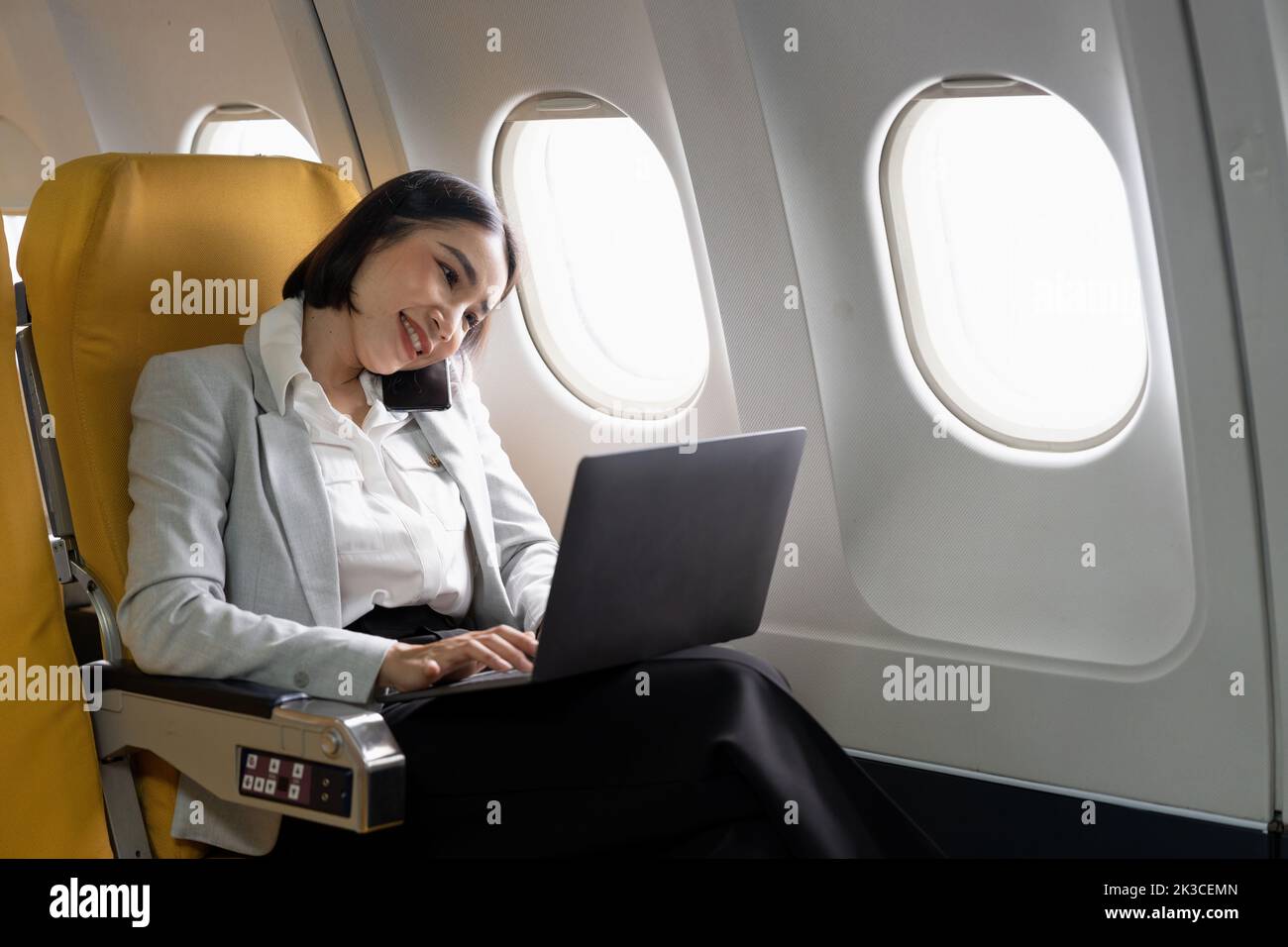 Cheerful asian businesswoman calling phone and using laptop computer during flight. Urban lifestyle Stock Photo