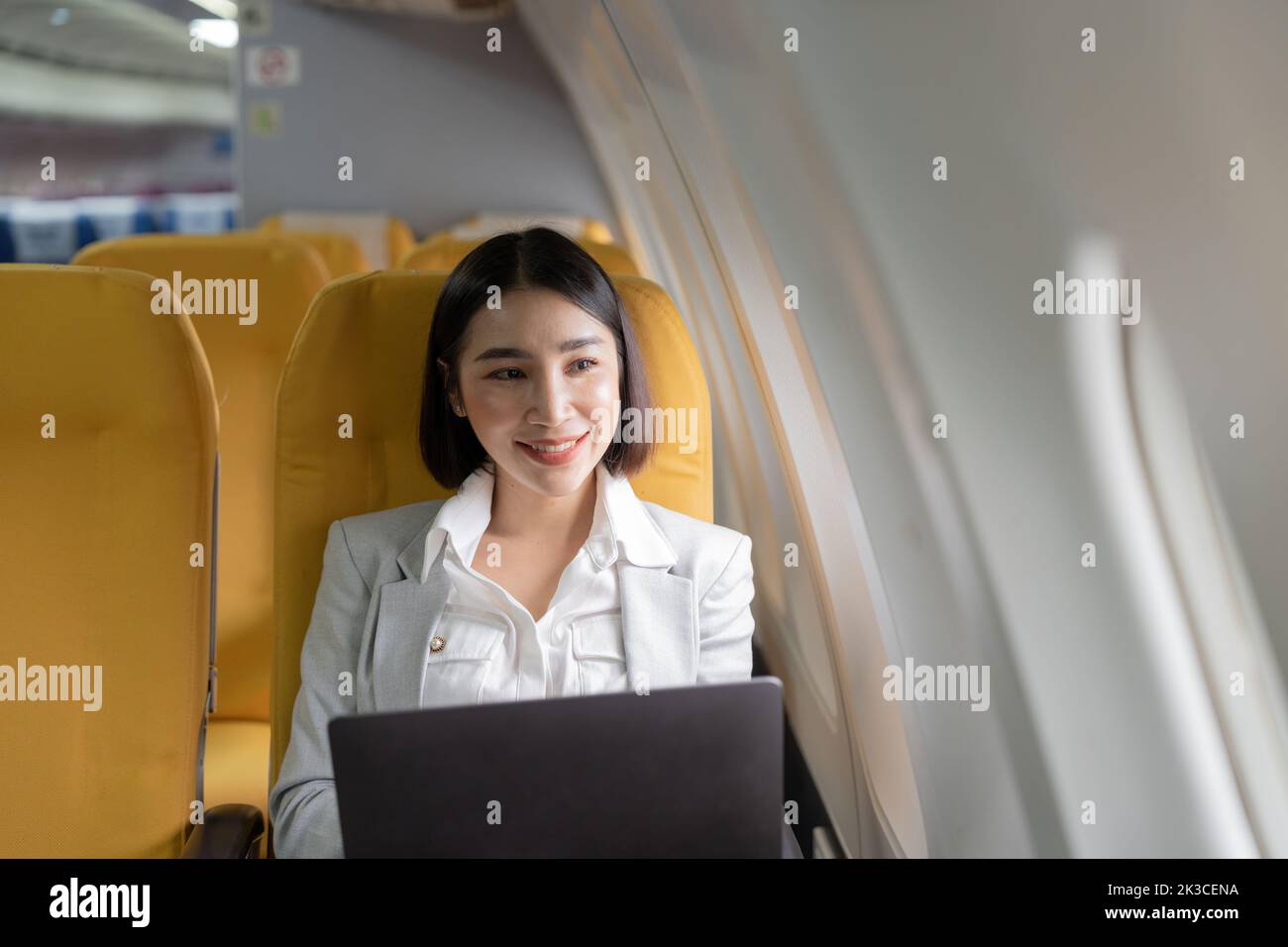 Traveling and technology. Flying at first class. Pretty young businees asian woman working on laptop computer while sitting in airplane. Stock Photo