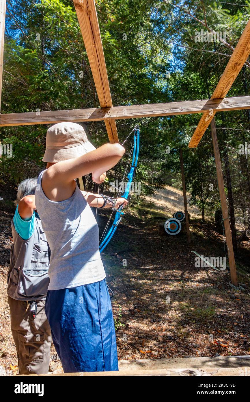 A boy trying archery, aiming an arrow at a target, bow drawn. Stock Photo
