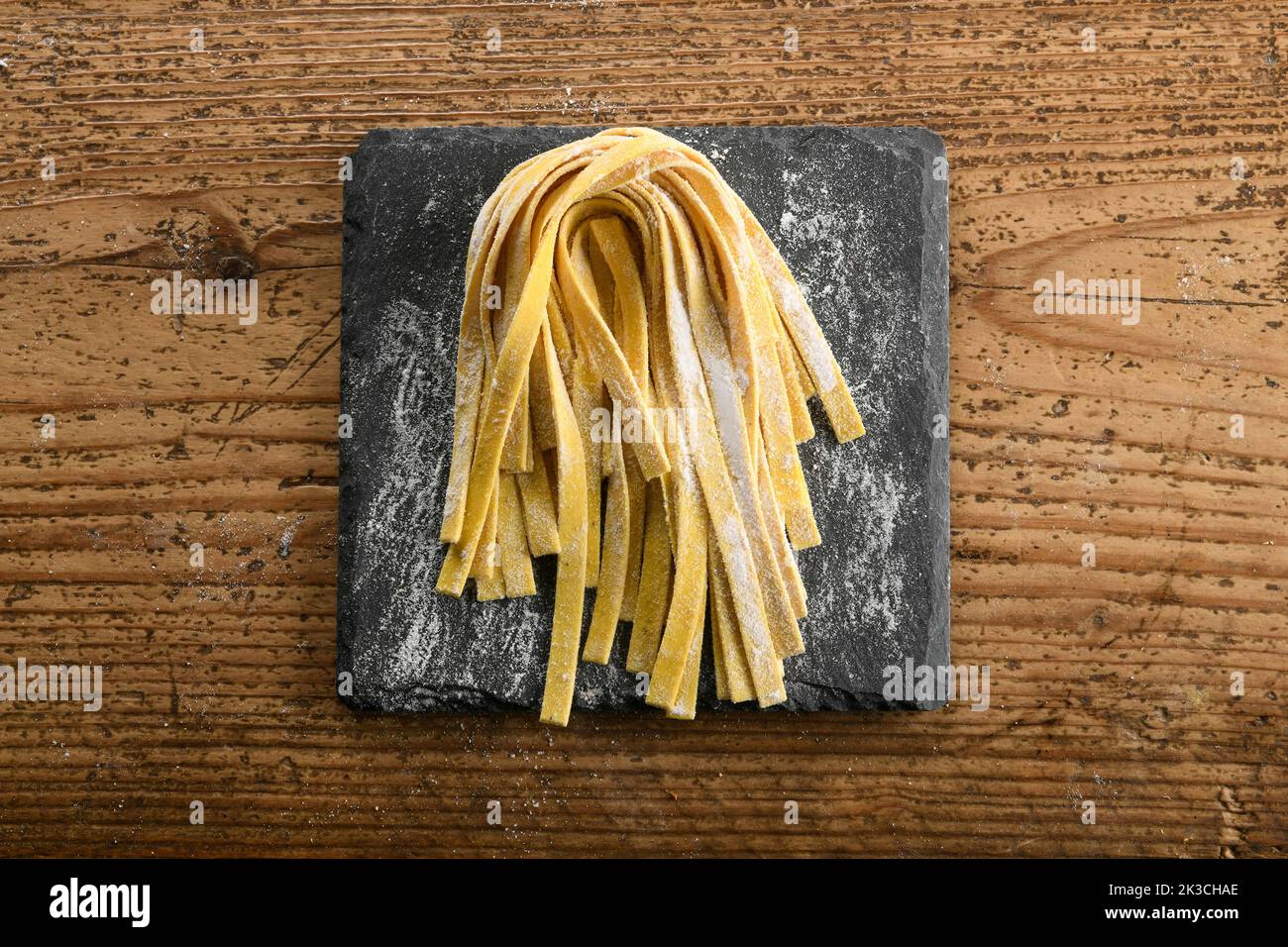 Top view of freshly prepared raw homemade Italian tagliatelle pasta with flour placed on slate board on wooden table in kitchen Stock Photo